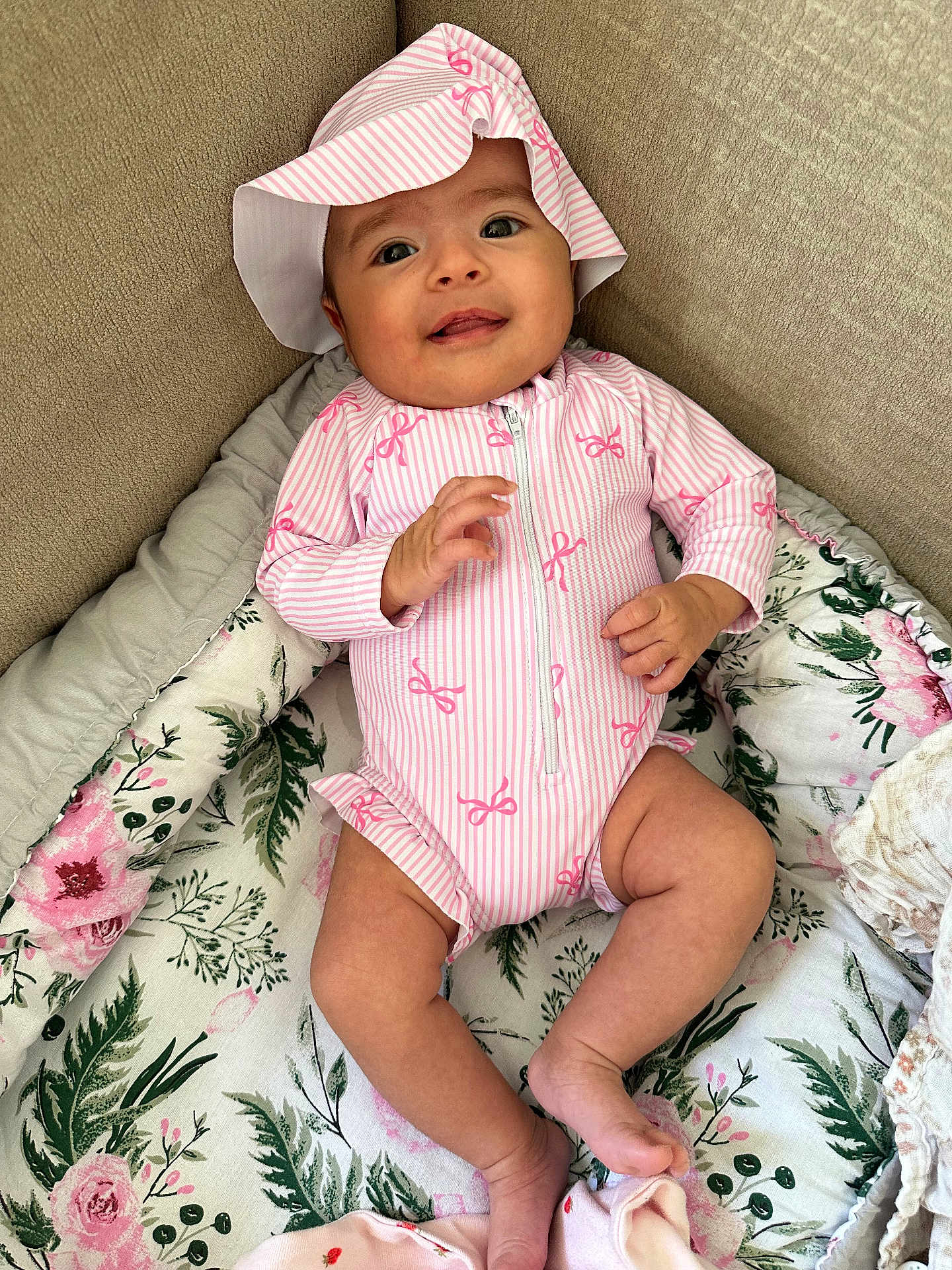 Alya a rejoint le concours — aidez-le/la à gagner de superbes lots ! baby, infant, smiling, hat, onesie, pink, floral_blanket, couch, cozy, hand, toes, eyes, portrait, indoor, fabric, pattern, zipper, headwear, soft_texture, relaxed