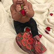 Louie is registered to the contest to win money with this photo: baby, child, rose, flower, valentines_day, heart_shaped_box, petals, blanket, smiling, happy, sitting, cute, indoor, infant, skin, black_pants, holiday, celebration, gift, person