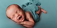 Tait is registered to the contest to win money with this photo: newborn, baby, sleeping, smiling, wrapped, blue_background, infant, cute, peaceful, soft_texture, portrait, child, skin, lying_down, tiny, happy, head, arm, hand, foot