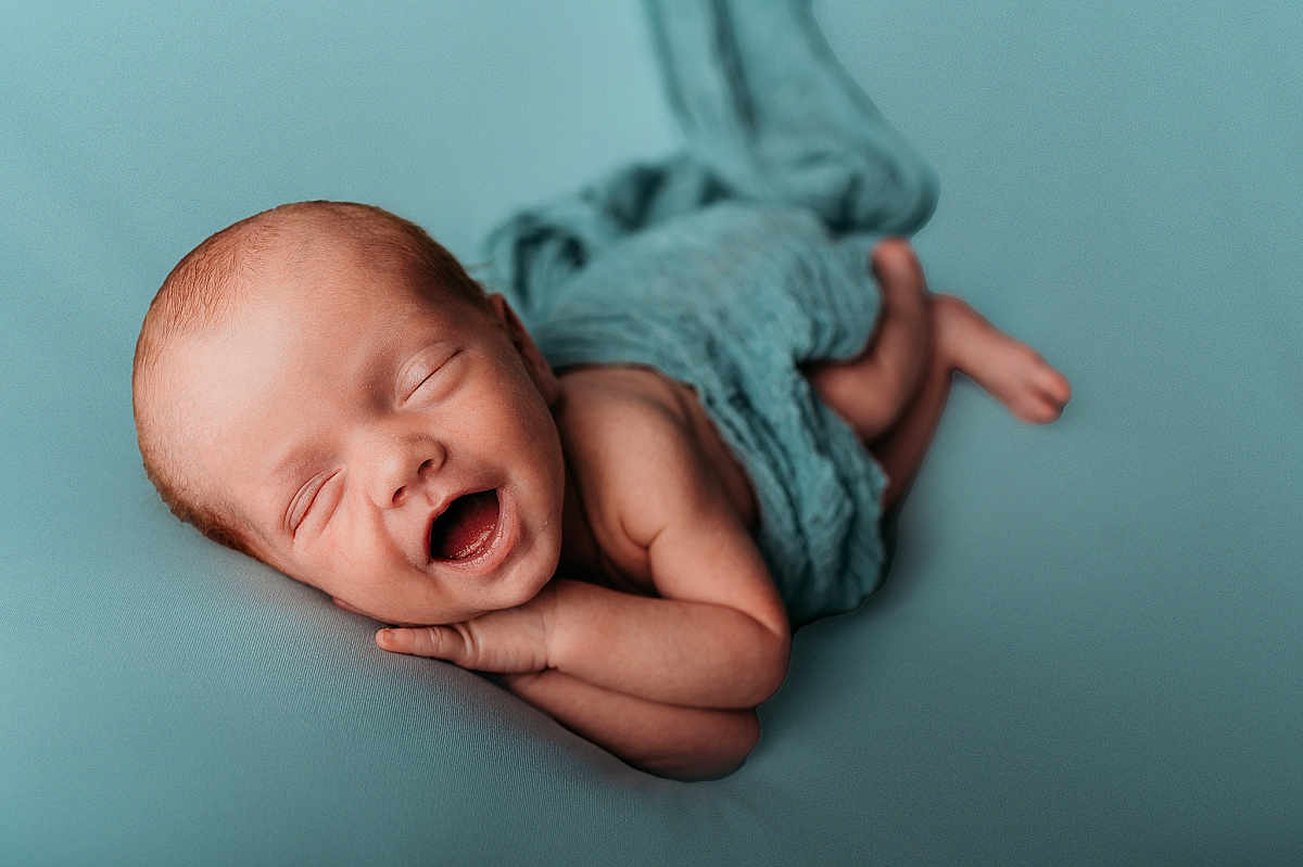 Tait is registered to the contest to win money with this photo: newborn, baby, sleeping, smiling, wrapped, blue_background, infant, cute, peaceful, soft_texture, portrait, child, skin, lying_down, tiny, happy, head, arm, hand, foot