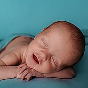 Tait is registered to the contest to win money with this photo: newborn, baby, sleeping, peaceful, closeup, portrait, infant, skin, hands, face, resting, blue_background, serene, smile, child, cute, young, soft, calm, lying_down