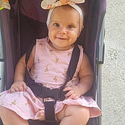 Apolline a rejoint le concours — aidez-le/la à gagner de superbes lots ! baby, child, stroller, smile, headband, pink_dress, flamingo_pattern, toy, purple_stroller, happy, cute, infant, sitting, outdoor, footrest, straps, baby_clothes, face, person, sunlight