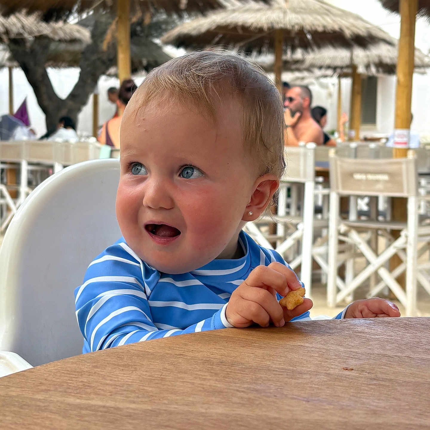 Sofia joined the competition — help win amazing prizes! baby, beach_umbrella, blue_eyes, casual, child, cute, daylight, eating, expression, high_chair, outdoor, people, portrait, restaurant, snack, striped_shirt, summer, table, toddler, wooden_table