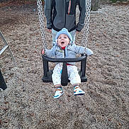 Kénaï participe au concours pour gagner de l'argent avec cette photo : adult, baby, chain, child, daytime, fence, fun, gravel, happy, hat, jacket, outdoor, park, person, playground, sneakers, support, swing, tree, winter_clothing