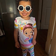 Braeleigh is registered to the contest to win money with this photo: child, toddler, smiling, sunglasses, curly_hair, pajamas, barefoot, indoor, colorful_clothing, cartoon_print, happy, portrait, standing, floor, wooden_floor, door, light, shadow, cute, playful