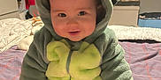 Austin joined the competition — help win amazing prizes! baby, child, dinosaur_onesie, hood, smile, sitting, bed, blanket, gloves, socks, indoor, cute, happy, face, person, clothing, cozy, soft, infant, portrait