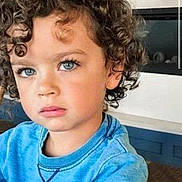Lucas joined the competition — help win amazing prizes! child, curly_hair, blue_eyes, sweatshirt, indoor, portrait, young_child, face, person, casual_clothing, modern_interior, fireplace, thoughtful, cute, kid, seated, expression, closeup, natural_light, hairstyle