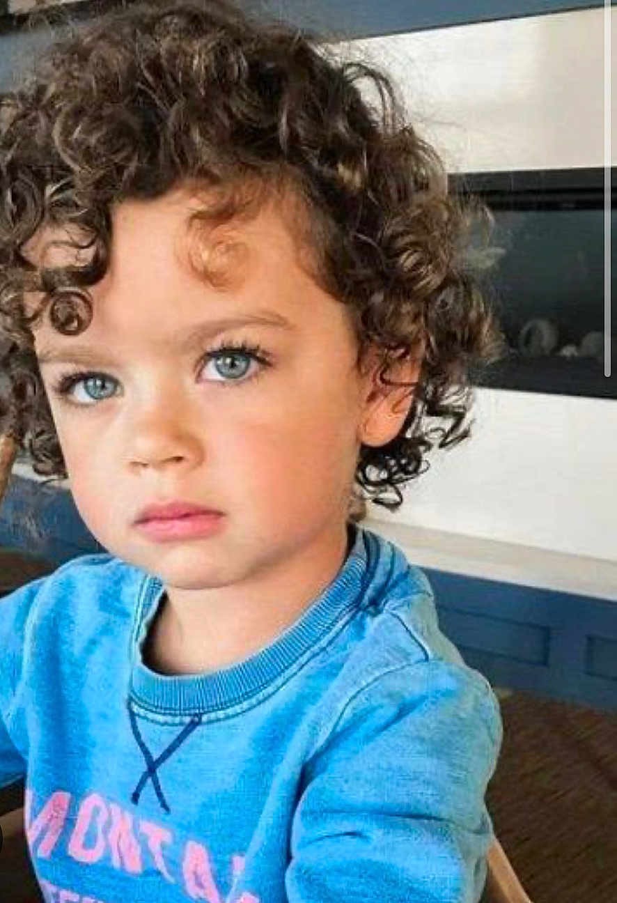 Lucas joined the competition — help win amazing prizes! child, curly_hair, blue_eyes, sweatshirt, indoor, portrait, young_child, face, person, casual_clothing, modern_interior, fireplace, thoughtful, cute, kid, seated, expression, closeup, natural_light, hairstyle