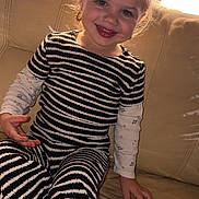 Carla a rejoint le concours — aidez-le/la à gagner de superbes lots ! child, smiling, couch, striped_clothing, long_sleeve_shirt, sitting, indoor, blonde_hair, blue_eyes, happy, toddler, cute, young_child, earrings, portrait, cozy, furniture, home, casual_clothing, natural_light