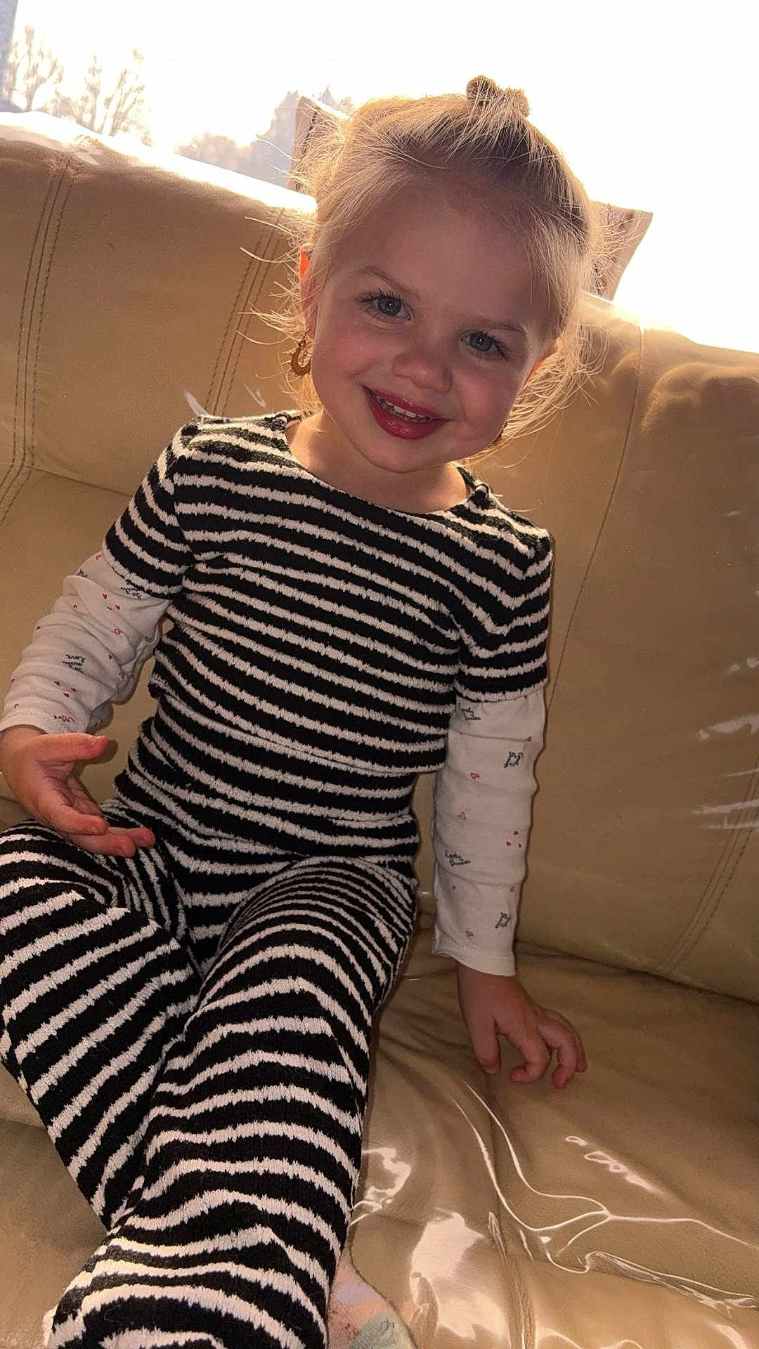 Carla a rejoint le concours — aidez-le/la à gagner de superbes lots ! child, smiling, couch, striped_clothing, long_sleeve_shirt, sitting, indoor, blonde_hair, blue_eyes, happy, toddler, cute, young_child, earrings, portrait, cozy, furniture, home, casual_clothing, natural_light