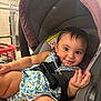 baby, child, car_seat, floral_dress, smile, curly_hair, straps, shopping_cart, indoor, person, seat, cute, infant, safety_harness, hand, foot, happy, closeup, expression, toddler