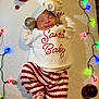 baby, sleeping, christmas, holiday, festive, lights, ornaments, red, white, striped_pants, sweater, hat, smiling, cute, infant, cozy, indoors, celebration, decoration, lying_down