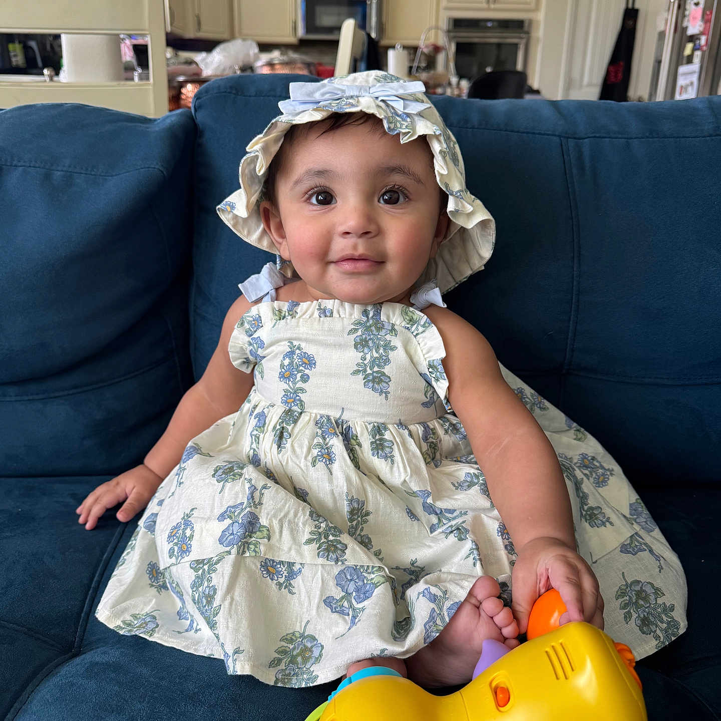 Anzal joined the competition — help win amazing prizes! blue, child, couch, curly_hair, dress, face, foot, furniture, happy, hat, indoor, kitchen, orange, person, plush, seated, smile, toddler, toy, yellow