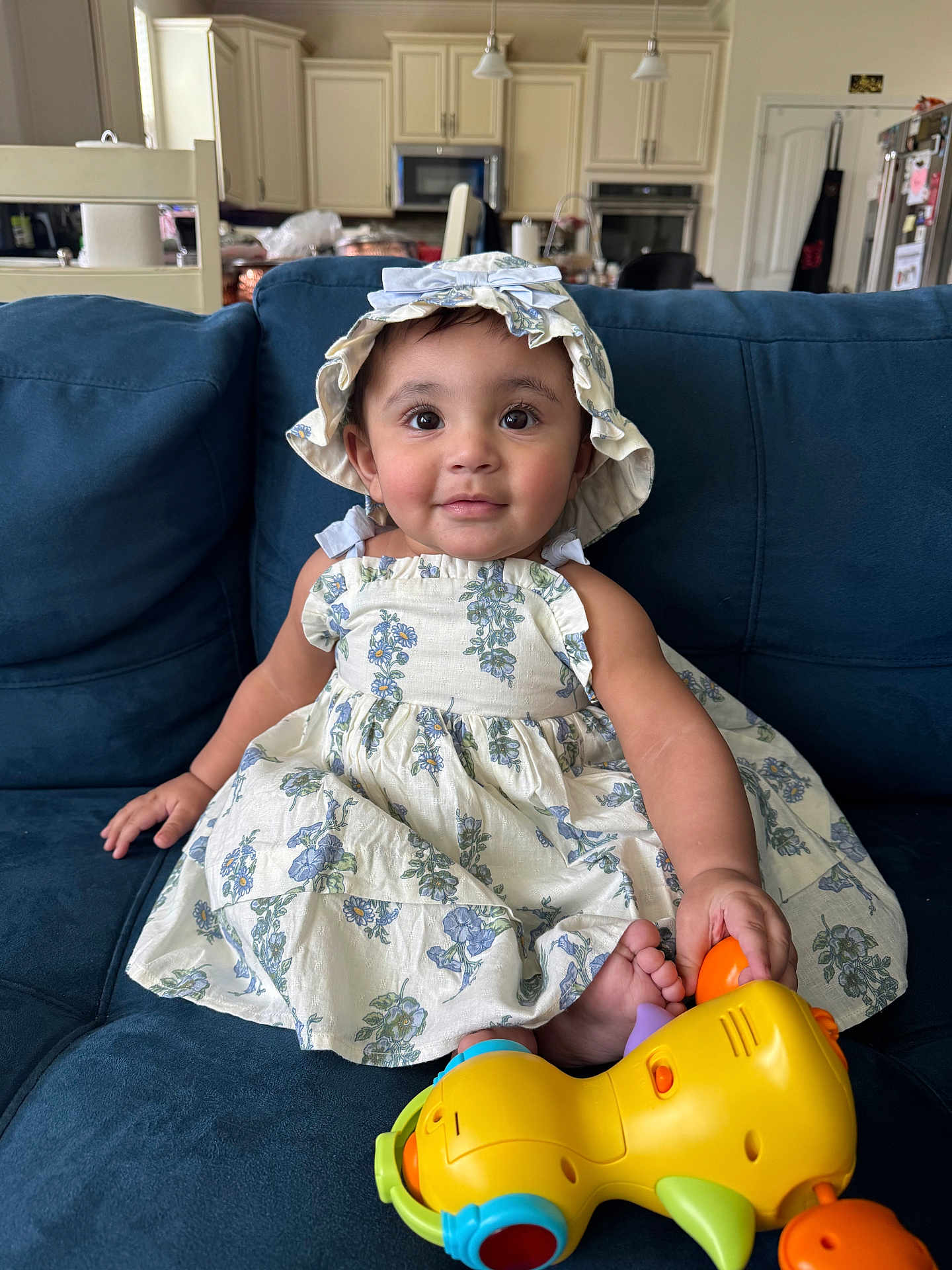 Anzal joined the competition — help win amazing prizes! toddler, child, dress, hat, toy, couch, indoor, kitchen, person, smile, face, foot, blue, yellow, orange, furniture, curly_hair, happy, seated, plush