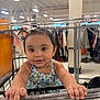 toddler, child, shopping_cart, store, clothing, retail, face, smile, baby, person, hand, hair_accessory, sleeveless_outfit, blue_flower_pattern, indoor, shopping, cute, happy, retail_store, holding