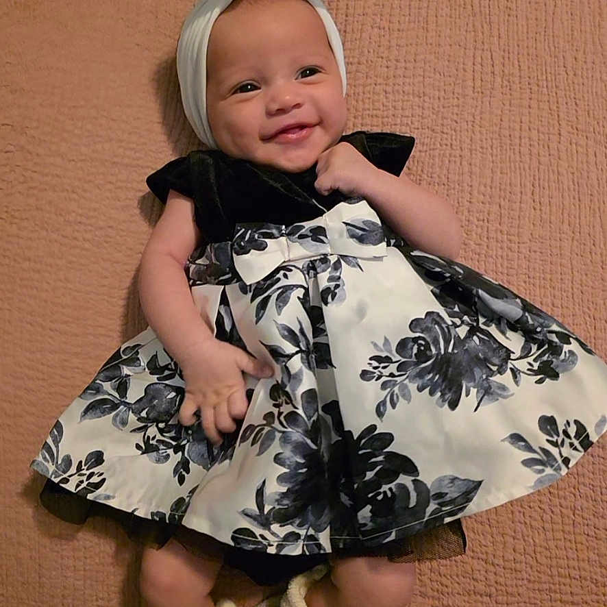 Tehani joined the competition — help win amazing prizes! adorable, apparel, baby, black_and_white, blanket, bow, child, cute, dress, fashion, floral, footwear, happy, headband, indoors, infant, lying_down, portrait, smiling, soft_texture