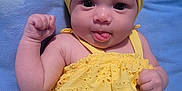 Tehani joined the competition — help win amazing prizes! baby, child, yellow_dress, headband, bow, tongue_out, fist, blue_blanket, cute, infant, smiling, portrait, lying_down, happy, skin, face, eyes, clothing, indoors, person
