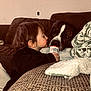 toddler, child, dog, bottle, couch, blanket, living_room, curious, face, pet, furniture, indoor, brown, cute, friendship, cozy, person, animal, black_clothing, home