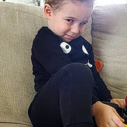ömer Alp is registered to the contest to win money with this photo: child, toddler, portrait, smiling, smirk, sitting, sofa, couch, indoors, home, black_clothing, curly_hair, barefoot, feet, family_photos, living_room, furniture, playful, close_up, natural_light