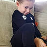 child, toddler, portrait, smiling, smirk, sitting, sofa, couch, indoors, home, black_clothing, curly_hair, barefoot, feet, family_photos, living_room, furniture, playful, close_up, natural_light