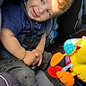 child, toddler, smiling, portrait, car_seat, vehicle, passenger, seatbelt, sunlight, indoor, toy, plush_toy, colorful, clothing, shoes, curly_hair, face, sitting, happy, photography