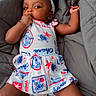 Kamarie is registered to the contest to win money with this photo: baby, child, infant, portrait, lying_down, blanket, bed, gray_blanket, bow, headband, dress, hawaiian_theme, colorful_clothing, smiling, looking_at_camera, hand_to_mouth, arms, legs, indoor, safe