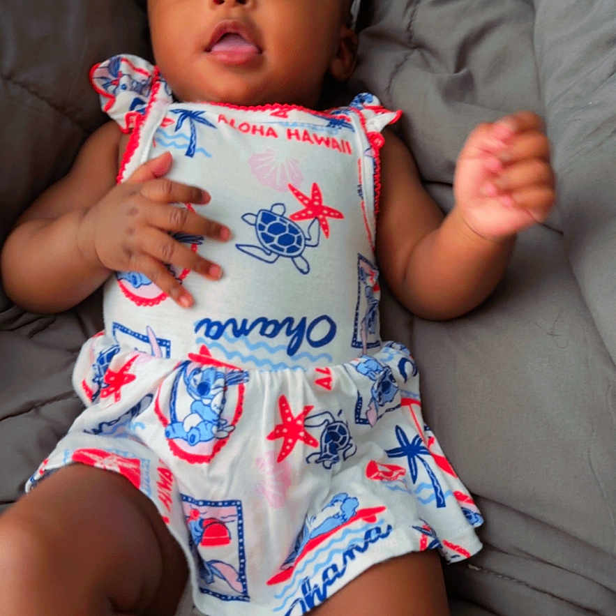 Kamarie joined the competition — help win amazing prizes! baby, infant, child, portrait, lying_down, bed, blanket, gray_background, bow, dress, tropical_pattern, colorful_clothing, smiling, face, eyes, hands, legs, indoor, cozy, photography