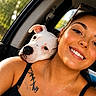 woman, dog, car_interior, selfie, smile, tattoo, necklace, black_tank_top, window, sunlight, pet, companion, happy, portrait, cute, friendship, closeup, relaxed, summer, road_trip