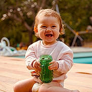 Jeanne participe au concours pour gagner de l'argent avec cette photo : toddler, child, smiling, sitting, green_cup, wooden_deck, outdoor, daylight, happy, short_hair, casual_clothing, diaper, nature, trees, pool, baby, cute, playful, person, portrait