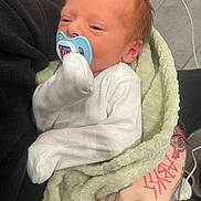 Jasper is registered to the contest to win money with this photo: newborn, baby, pacifier, blanket, tattoo, hand, infant, white_clothing, sleepy, face, skin, person, holding, nail_polish, black_nails, indoor, closeup, soft_texture, cute, resting