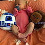 baby, chewbacca, child, comfortable, curious, cute, floral_pattern, indoors, infant, lying_down, newborn, orange_blanket, pacifier, pink_onesie, plush_toy, r2d2, resting, small_feet, soft_toys, star_wars