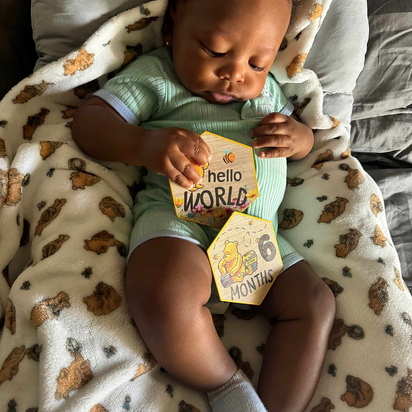 Baby Eli is registered to the contest to win money with this photo: baby, blanket, brown_skin, cardboard_sign, cozy, cute, face, hand, indoors, infant, legs, lying_down, milestone_card, nursery, onesie, portrait, sleepy, socks, soft_texture, teddy_pattern