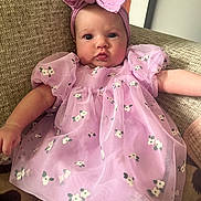 Sadie is registered to the contest to win money with this photo: baby, infant, child, pink_dress, headband, bow, floral_pattern, puffed_sleeves, couch, textured_fabric, indoor, portrait, cute, puckered_lips, relaxed, person, seated, soft_lighting, close_up, adorable