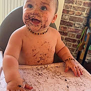 Louka a rejoint le concours — aidez-le/la à gagner de superbes lots ! baby, high_chair, chocolate, messy, smiling, happy, face, hands, table, food, indoor, child, cute, playful, dirt, skin, necklace, expression, toddler, mess