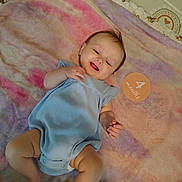 Brenda is registered to the contest to win money with this photo: baby, infant, smiling, blue_outfit, blanket, pastel_colors, lying_down, cute, child, young, indoor, happy, four_months, sign, skin, face, legs, hand, cozy, soft