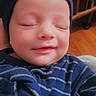 Grayson is registered to the contest to win money with this photo: baby, smiling, closed_eyes, blue_clothing, striped, hat, infant, cozy, sleepy, portrait, child, cute, indoor, wooden_background, warm, soft_light, person, newborn, sleeping, happy