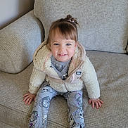 Journee is registered to the contest to win money with this photo: child, smiling, sitting, couch, indoor, clothing, jacket, pants, sneakers, floor, hair, person, happy, footwear, young_child, cozy, home, casual, portrait, furniture