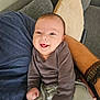 Charlie is registered to the contest to win money with this photo: baby, infant, smile, happy, person, clothing, gray_shirt, pants, couch, pillow, arm, bracelet, skin, face, indoor, comfort, joy, cute, small_hands, seated