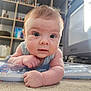 baby, infant, tummy_time, carpet, curious, blue_eyes, indoor, furniture, bookshelf, toy, child, person, face, skin, hair, cute, portrait, expression, home, floor