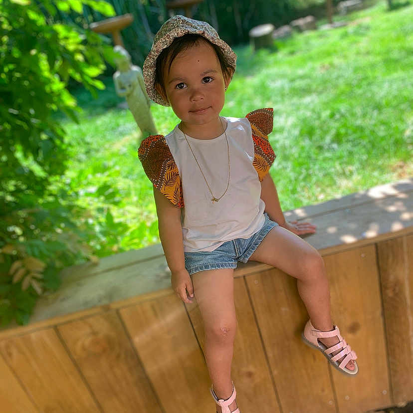 Imaïny a rejoint le concours — aidez-le/la à gagner de superbes lots ! child, clothing, face, female, footwear, girl, grass, hat, head, pants, person, photography, plant, portrait, pottedplant, sandal, shoe, shorts, sitting, wood