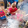 child, adult, fire_pit, smoke, water, outdoor, autumn, leaves, red_jacket, blue_clothing, learning, supervision, playgroup, curiosity, nature, hands, bucket, rope, glasses, face_mask