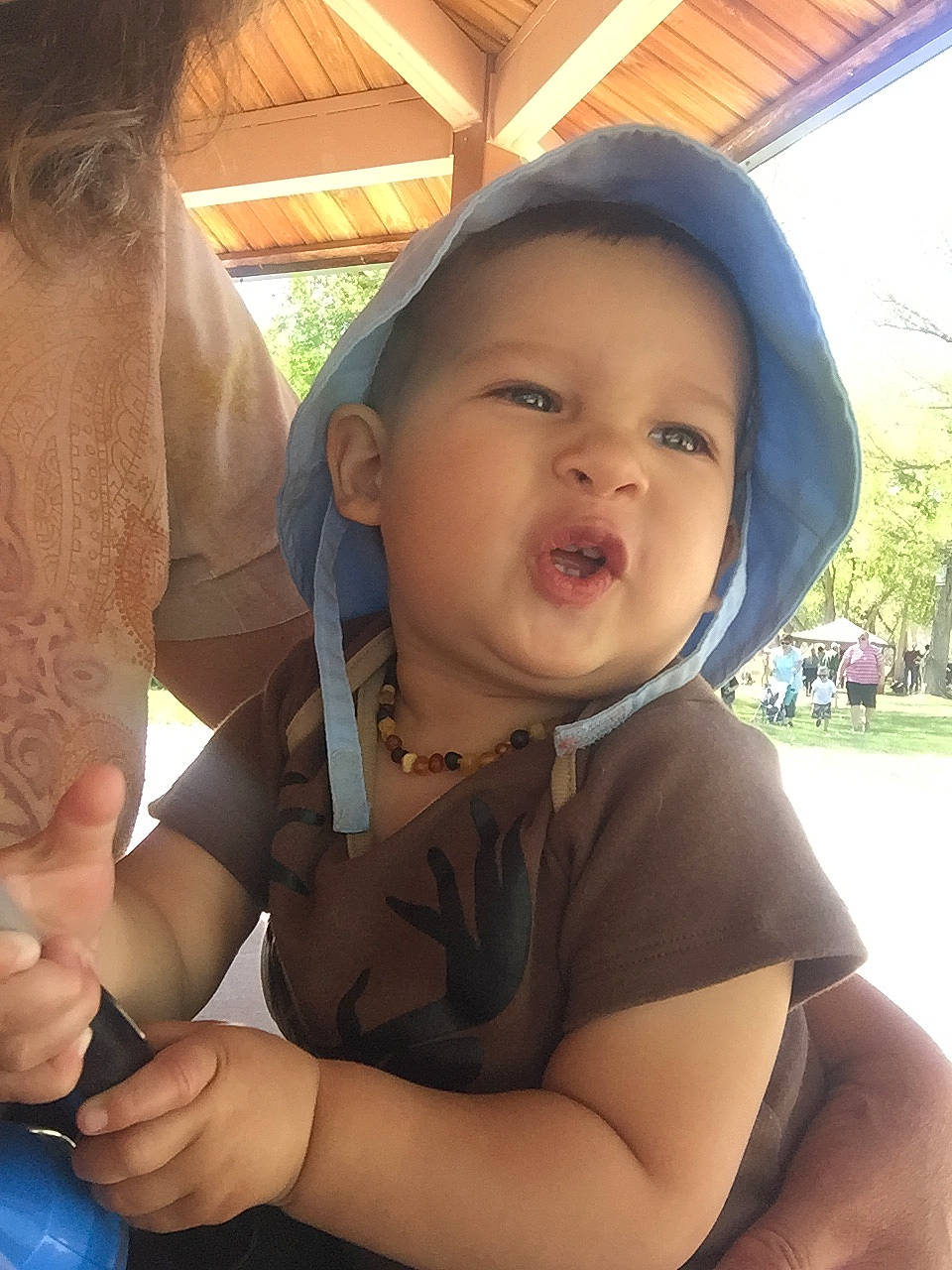 Silas is registered to the contest to win money with this photo: baby, child, finger, fun, gesture, grass, hairstyle, happy, hat, headwear, leisure, nose, person, plant, shoulder, sitting, skin, t_shirt, thumb, toddler