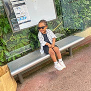 Venus participe au concours pour gagner de l'argent avec cette photo : child, sunglasses, bench, bus_stop, greenery, glass_panel, casual_clothing, sneakers, smile, outdoor, paper_bag, asphalt, hairstyle, street, public_transport, person, young, daylight, relaxed, urban