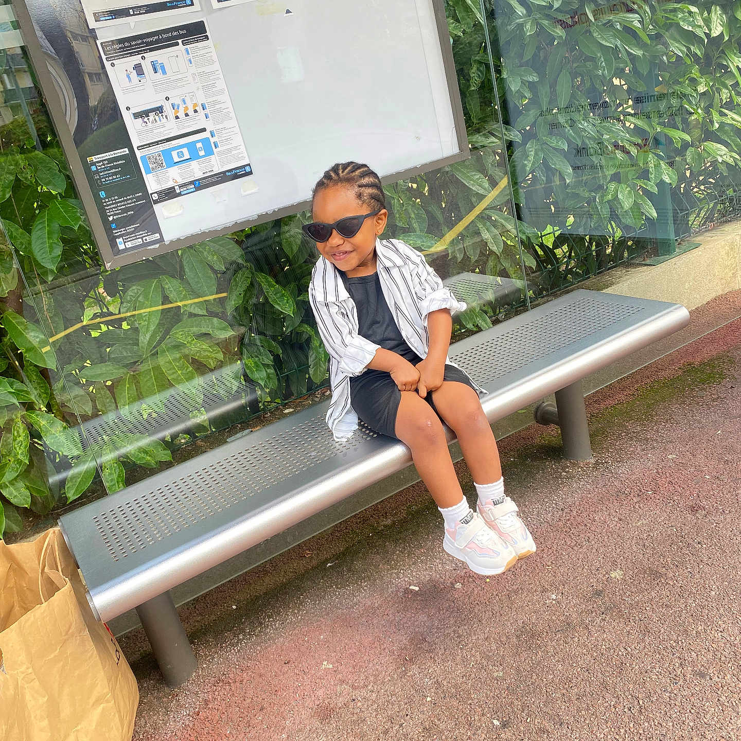 Venus participe au concours pour gagner de l'argent avec cette photo : asphalt, bench, bus_stop, casual_clothing, child, daylight, glass_panel, greenery, hairstyle, outdoor, paper_bag, person, public_transport, relaxed, smile, sneakers, street, sunglasses, urban, young