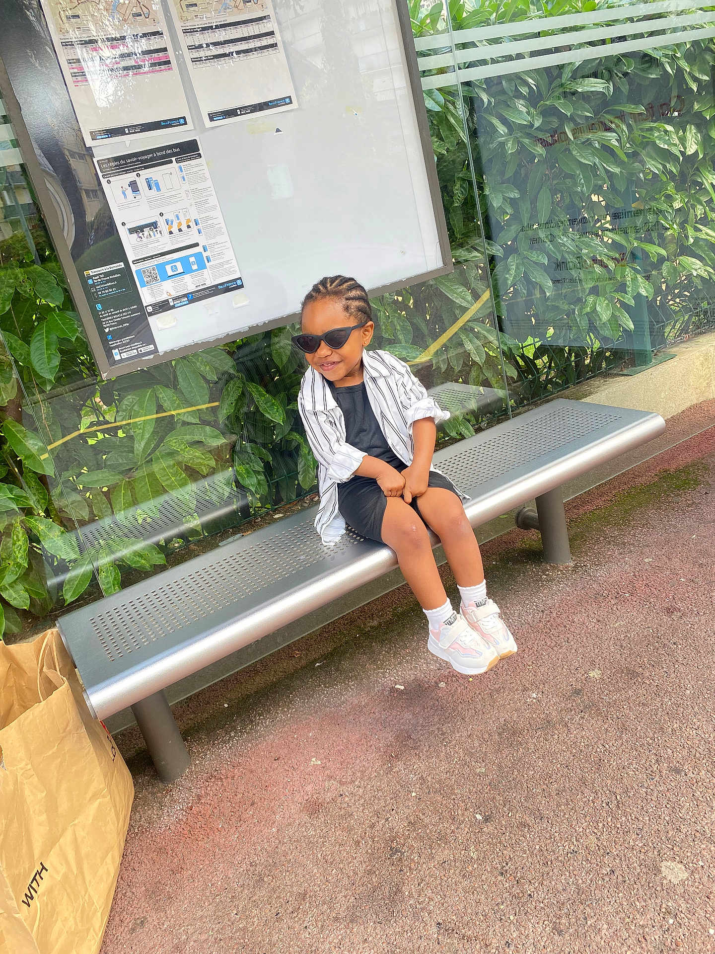 Venus participe au concours pour gagner de l'argent avec cette photo : child, sunglasses, bench, bus_stop, greenery, glass_panel, casual_clothing, sneakers, smile, outdoor, paper_bag, asphalt, hairstyle, street, public_transport, person, young, daylight, relaxed, urban