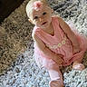 baby, child, pink_dress, headband, flower, carpet, sitting, cute, indoor, portrait, person, toddler, soft, texture, floor, clothing, smile, young, happy, looking_up