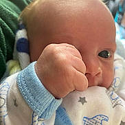 Waylon is registered to the contest to win money with this photo: baby, newborn, infant, hand, fist, face, eye, onesie, pajamas, star_pattern, blue_trim, blanket, soft_skin, close_up, portrait, cradled, eyelash, cheek, indoors, cute