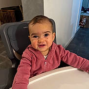 Sïana participe au concours pour gagner de l'argent avec cette photo : baby, child, high_chair, pink_hoodie, smiling, indoor, face, person, table, happy, cute, young_child, seated, clothing, expression, head, room, furniture, skin, portrait