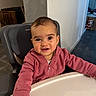 baby, child, high_chair, pink_hoodie, smiling, indoor, face, person, table, happy, cute, young_child, seated, clothing, expression, head, room, furniture, skin, portrait