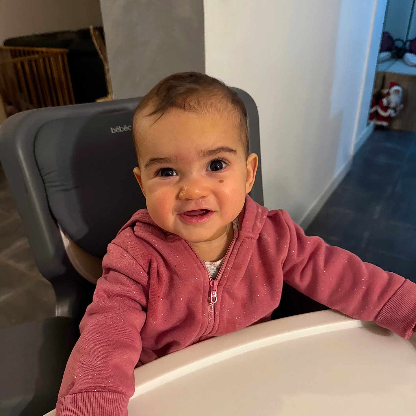 Sïana participe au concours pour gagner de l'argent avec cette photo : baby, child, high_chair, pink_hoodie, smiling, indoor, face, person, table, happy, cute, young_child, seated, clothing, expression, head, room, furniture, skin, portrait